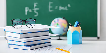 Bücher, Brille und Stifte vor Tafel mit mathematischen Formeln