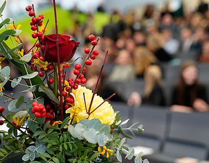 Blick auf einen Blumenstrauß mit Publikum im Hintergrund bei der feierlichen Verabschiedung der Absolventinnen und Absolventen 2023 des Fachbereichs WIR