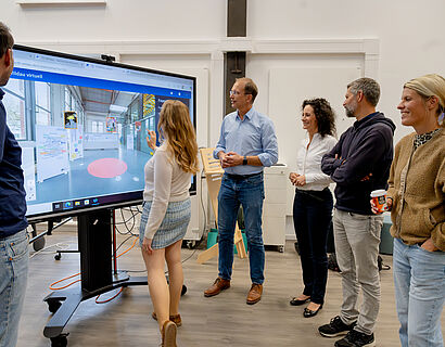 Sechs Personen stehen an einem großen Monitor, eine Person steht vorne und bedient den Touchscreen.