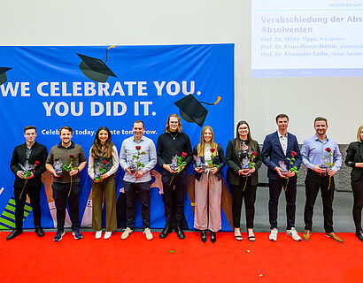 Absolvent*innen bei einem Gruppenbild vor einer Plakatwand