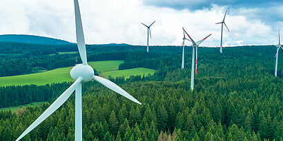 Windkraftanlagen zwischen Bäumen und Feldern