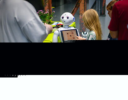 Ein Kind steht vor einem humanoiden Roboter und bedient das Display