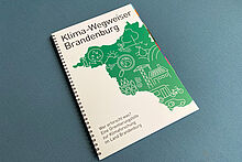 Klima-Wegweiser Brandenburg Broschüre mit der Aufschrift "Klimawegweiser Brandenburg" auf einem türkisfarbenen Hocker