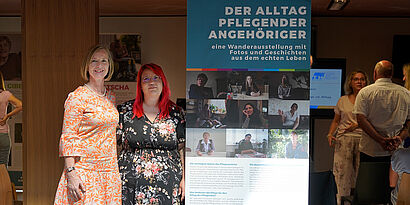 Zwei Frauen stehen neben einem Rollup mit der Aufschrift "Der Alltag pflegender Angehöriger"