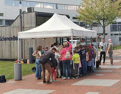 Kinderuni Summer Edition 2025 - Kids stehen vor einem Pavillion auf dem Campus und freuen sich auf ein Eis 