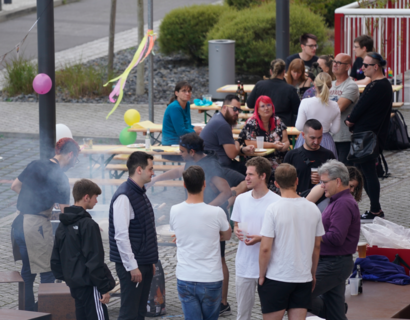 Menschen sitzen und stehen an Bierbänken und unterhalten sich